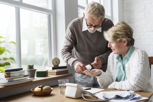 An older couple examines a prescription bottle, discussing its contents with concern and care in their expressions.