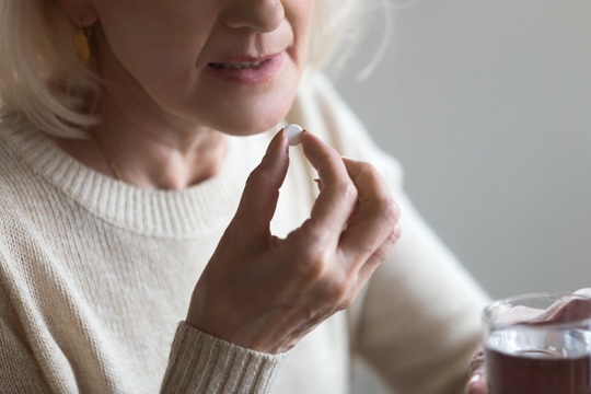 A woman with a pill in her hand, illustrating a moment of contemplation regarding her health choices.