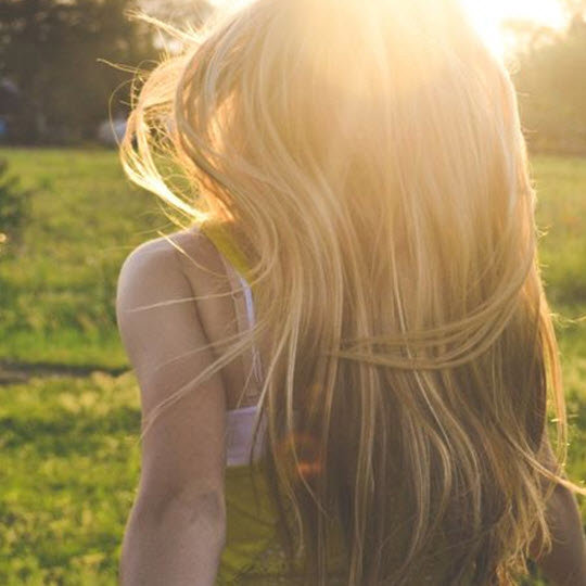 A woman with long blonde hair strolls under the bright sun, enjoying a warm and radiant day outdoors.