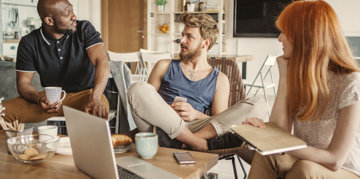 A group of three people around a table, focused on their laptops, likely working together on a project.