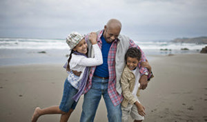 An older gentleman plays on the beach with two children, capturing a moment of happiness and togetherness by the ocean.