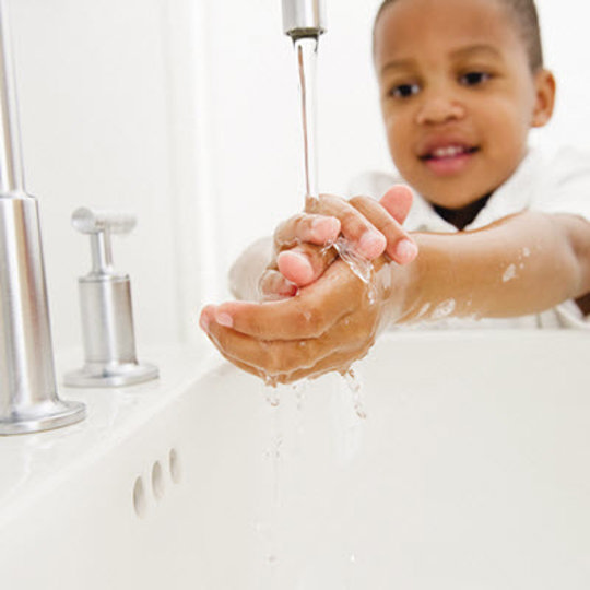 A young boy stands at a sink, diligently washing his hands with soap and water, promoting good hygiene practices.