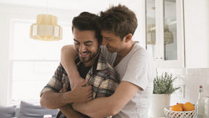 Two men share a joyful hug in a kitchen, capturing a moment of affection and friendship in a familiar environment.