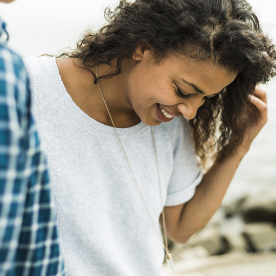 A woman and a man stand side by side, both smiling, in a friendly and relaxed outdoor setting.