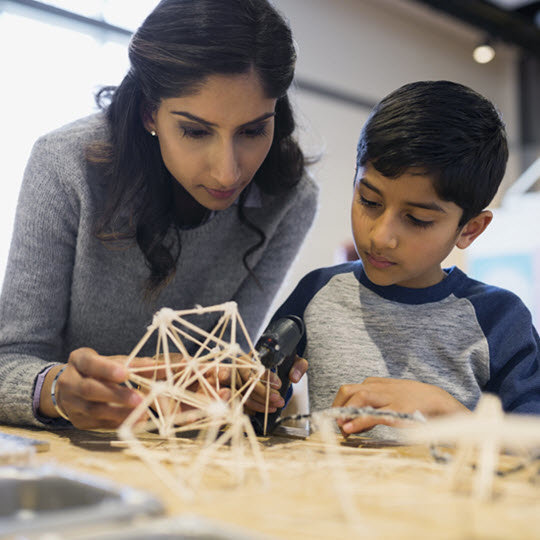 A woman and a boy collaboratively building a model structure, showcasing teamwork and creativity in their project.