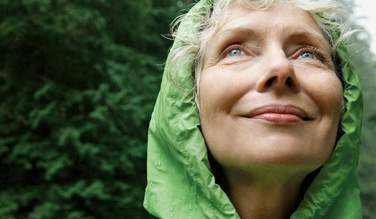 A woman in a green raincoat smiles brightly, showcasing her cheerful demeanor despite the rainy weather.