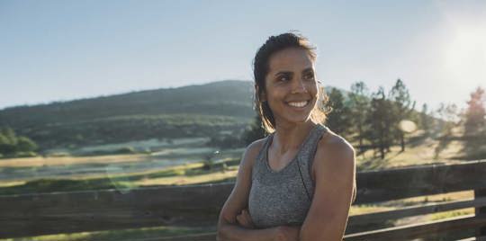 A cheerful woman stands against a backdrop of towering mountains