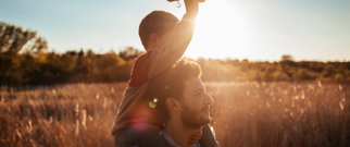 Man with depression walking through a field with child on his shoulders-hero-banner