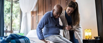 Woman helping her elderly father up from the bed